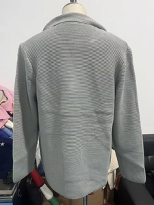 Detail view of the heavy knit texture and ribbed hem of a gray men's cardigan
