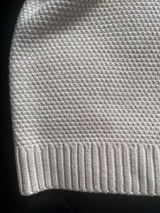 Detailed macro view of light gray waffle knit texture and ribbed hem on a sweater