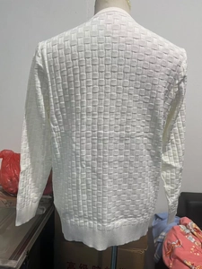 Close-up of white long sleeve knit sweater featuring textured waffle pattern fabric