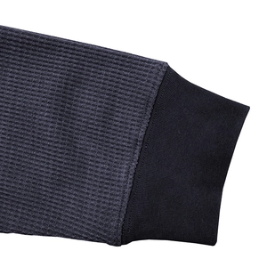 Close-up of dark grey waffle knit fabric texture and ribbed cuff on long sleeve shirt