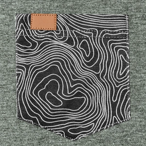 Détail de la poche poitrine avec motif topo blanc et patch en cuir marron sur le débardeur