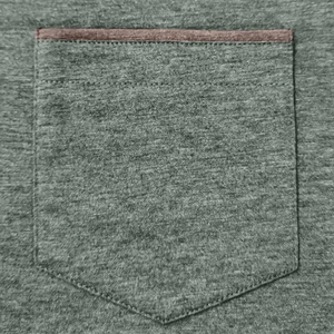 Detailed close-up of the front chest pocket with brown faux leather trim on a polo shirt