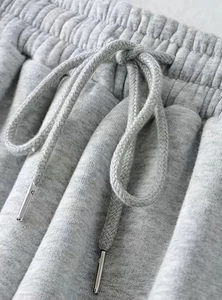 Dettaglio dei joggers grigi con elastico in vita e coulisse con punte in metallo argento