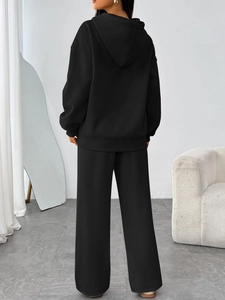 Rear view of a black women's oversized hoodie and wide-leg sweatpants set in a modern room