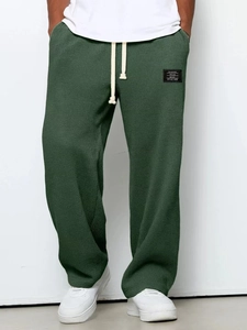 Dettaglio dei pantaloni in maglia a nido d'ape verde scuro con coulisse bianca e patch