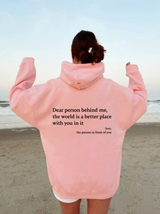 Rear view of an oversized pink fleece hoodie with black text print on a beach
