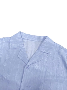 Detailed close-up of light blue Cuban collar shirt with textured fabric and resin button