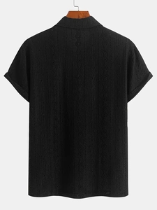 Détail d'un polo en maille noir avec texture diamant ajourée et revers de manches
