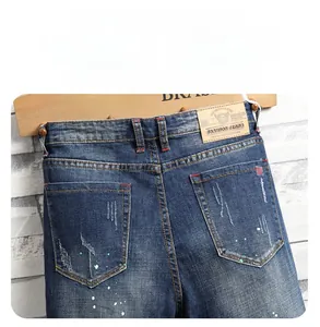 Detailed view of dark blue jeans featuring distressing, splatter paint, and a leather waist tag