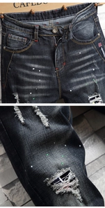 Detail der dunkel gewaschenen Jeans mit Farbspritzern, Rissen und strapazierter Denim-Textur