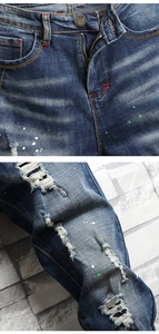 Detail of blue distressed denim with green paint splatters and red contrast stitching
