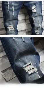 Detail of distressed dark blue jeans with green paint splatters and red thread accents