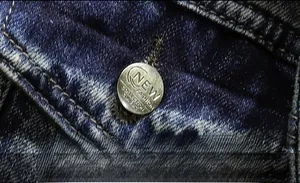 Detailed close-up of a silver metal button with classic engraving on blue washed denim fabric