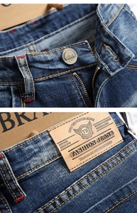 Detail of dark blue denim jeans showing metal button and brown leather brand patch