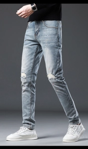 Detail of light blue distressed jeans featuring colorful paint splatters and ripped knee design