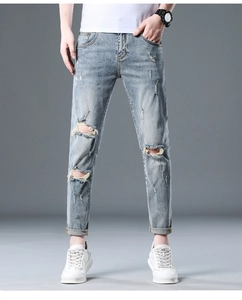 Detail view of men's light blue distressed jeans with knee rips and whiskers
