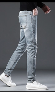 Detailed side view of slim fit light blue washed denim jeans with distressed knee holes