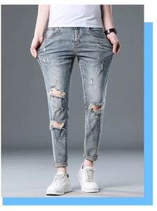 Detailed close-up of light blue distressed denim jeans with ripped knees and whiskers