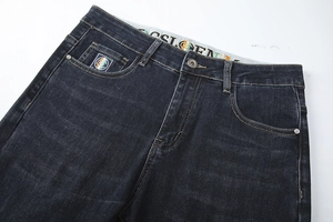 Detailed close-up of men's dark denim jeans waist with metal button and woven logo
