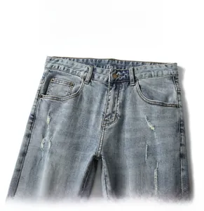 Detailed close-up of light blue distressed denim jeans with frayed holes and cat whiskers