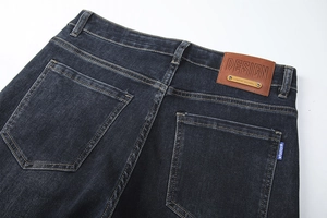 Detail view of dark wash denim jeans with a brown leather patch and rear pocket stitching