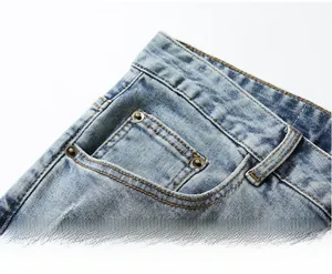 Detail of ripped blue denim jeans showing the deep front pocket and metal rivets