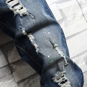 Slim fit men's distressed blue denim jeans with paint splatters and ripped details