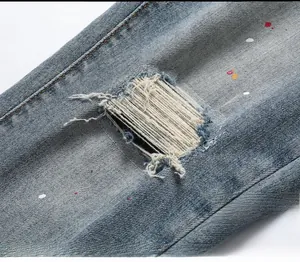 Detail of distressed blue denim jeans with ripped holes and colorful paint splatters