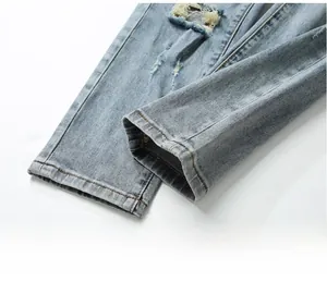 Detail of distressed hem and ripped design on light blue men's slim fit denim jeans
