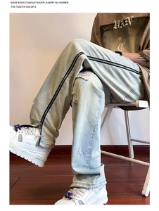 Detail of light blue washed denim jeans with side zipper and distressed knee rip