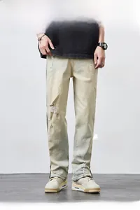 Detail of light wash distressed jeans featuring vintage rips and raw hem on straight leg fit