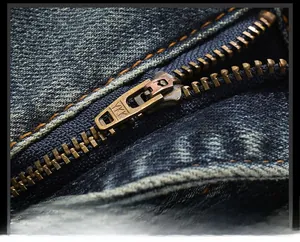 Macro d'une fermeture éclair YKK en bronze et coutures jaunes sur un jean délavé
