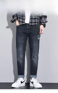 Detail shot of men's dark blue jeans featuring cuffed hems and white embroidery details