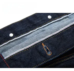 Macro detail of dark indigo selvedge denim fabric with orange stitching and vintage button
