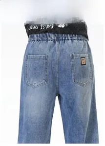 Détail du jean bleu clair montrant la taille élastique et une broderie numéro 7 sur la poche