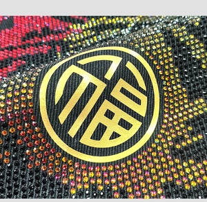 Detail of colorful gradient rhinestones with a gold Fu character emblem on black fabric