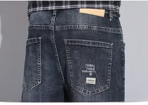 Detail view of dark blue jeans featuring rear pocket embroidery and a brown leather patch