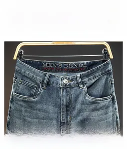 Detail of men's blue washed denim jeans showing waist button and embroidered inner logo