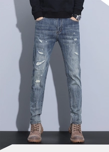 Detail of blue slim fit men's jeans featuring distressed knee holes and white paint splatters