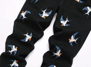 Close-up of vibrant swallow bird embroidery on premium black stretch denim jeans
