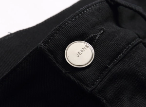 Macro detail of silver metal button with JEANS engraving on black denim waist