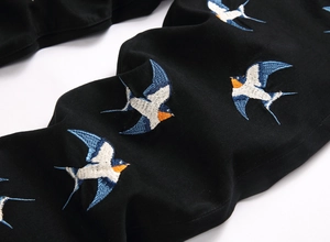 Macro view of detailed blue, white and orange swallow embroidery on black denim fabric