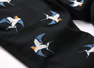 Close-up of colorful bird embroidery on black slim fit denim fabric for men pants