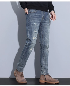 Detail of distressed ripped denim with white paint splatter on blue men's slim jeans