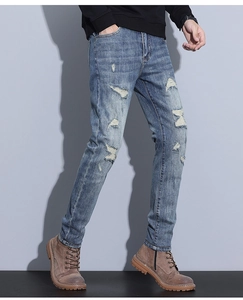 Detailed view of light blue distressed denim jeans with handmade ripped hole details