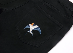 Detailed embroidery of colorful swallow birds on the back pocket of black denim jeans