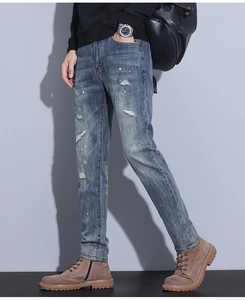Detail of blue slim fit men's jeans featuring distressed holes and white paint splatter accents