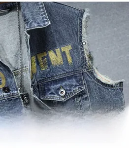 Close-up of frayed armhole detail and yellow ENT embroidery on a blue denim vest