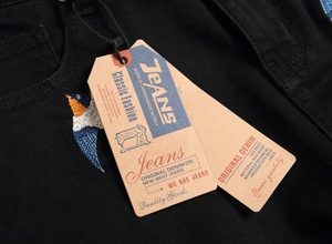Detailed close-up of colorful swallow embroidery and vintage tags on black denim pants