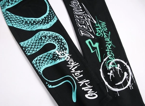 Detail of black slim jeans with green graffiti print and streetwear typography text